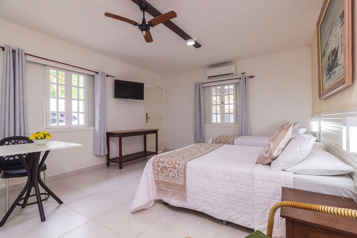 Habitación de hotel con cama, escritorio, silla, ventilador de techo y un cuadro en la pared.