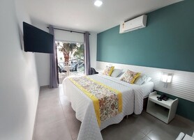 Una habitación de hotel con cama, una mesita de noche con teléfono, un televisor montado en la pared y vistas al exterior.