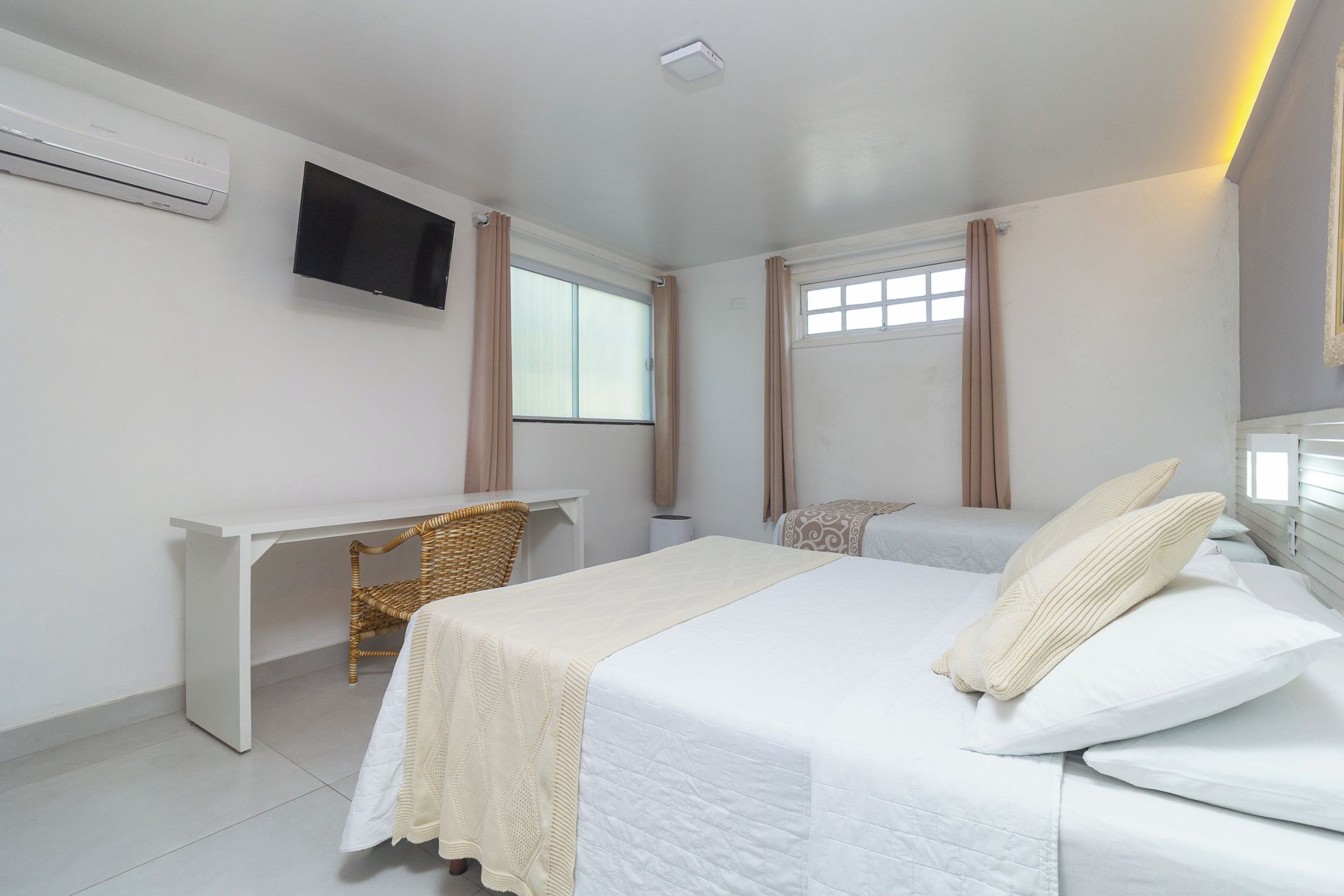 A hotel room with a bed, a desk, a television, and windows with curtains.