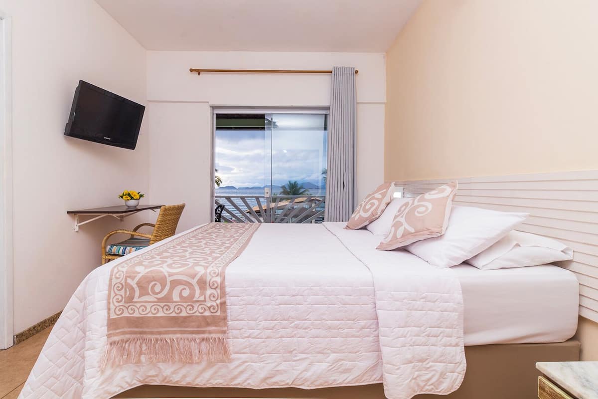 Un dormitorio con cama, televisión, balcón con vistas y una pequeña mesa con una planta.