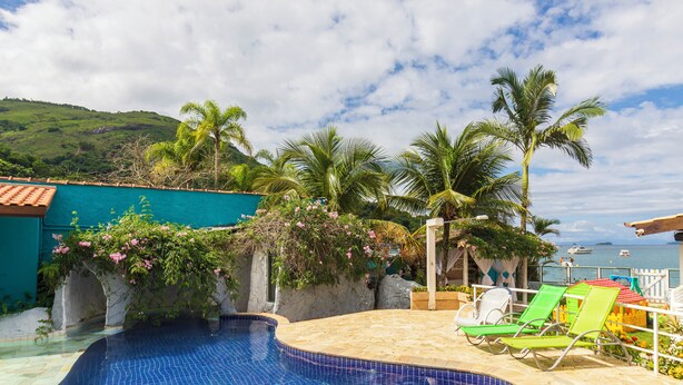 A swimming pool with tiled blue floor, surrounded by palm trees and a view of the sea. - Pousada Daleste (Angra dos Reis)