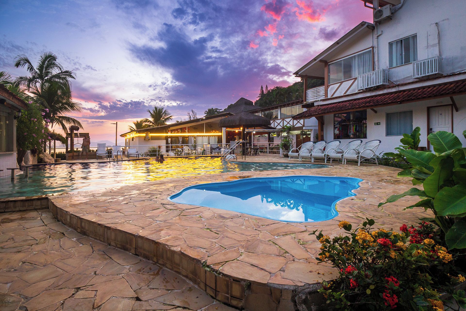 Piscina com espreguiçadeiras e vista para o pôr do sol.