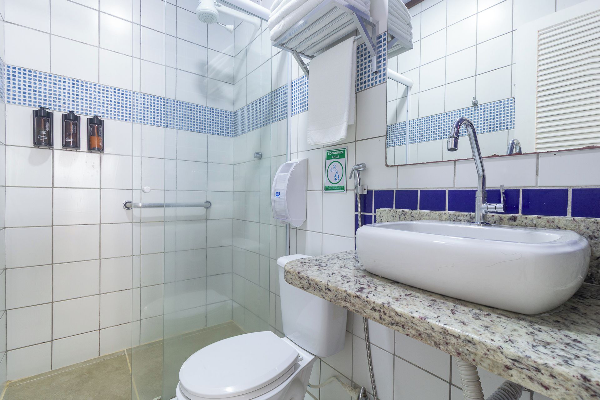 Un baño con inodoro blanco, lavamanos con encimera de mármol y zona de ducha.