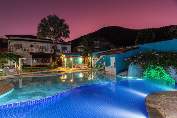 A swimming pool with clear blue tiles, surrounded by buildings and palm trees. - Pousada Daleste (Angra dos Reis)