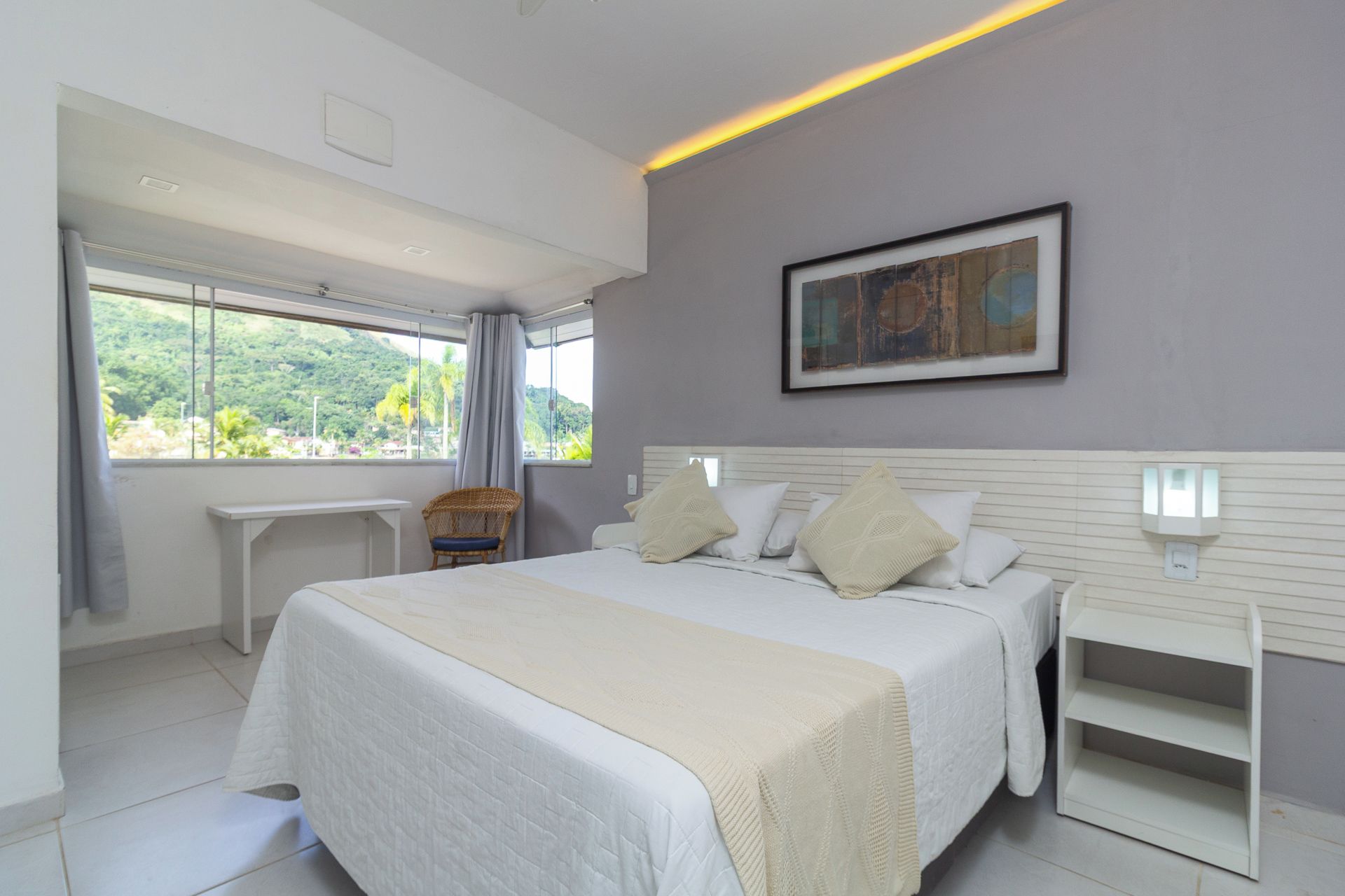 A modern bedroom with a large bed, bedside tables, a chair, and a painting on the wall.