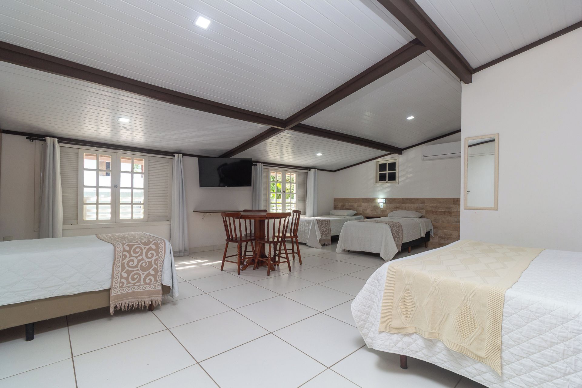 Una habitación con dos camas, una mesa con sillas, un televisor y un ventanal con cortinas.