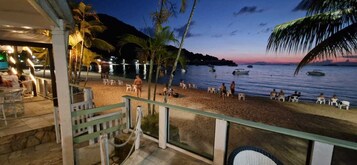 A beachside view with a balcony overlooking the sea, palm trees, and boats.