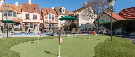 Un campo de golf bien cuidado con un putting green, rodeado de edificios de estilo europeo tradicional con fachadas de ladrillo y techos a dos aguas.