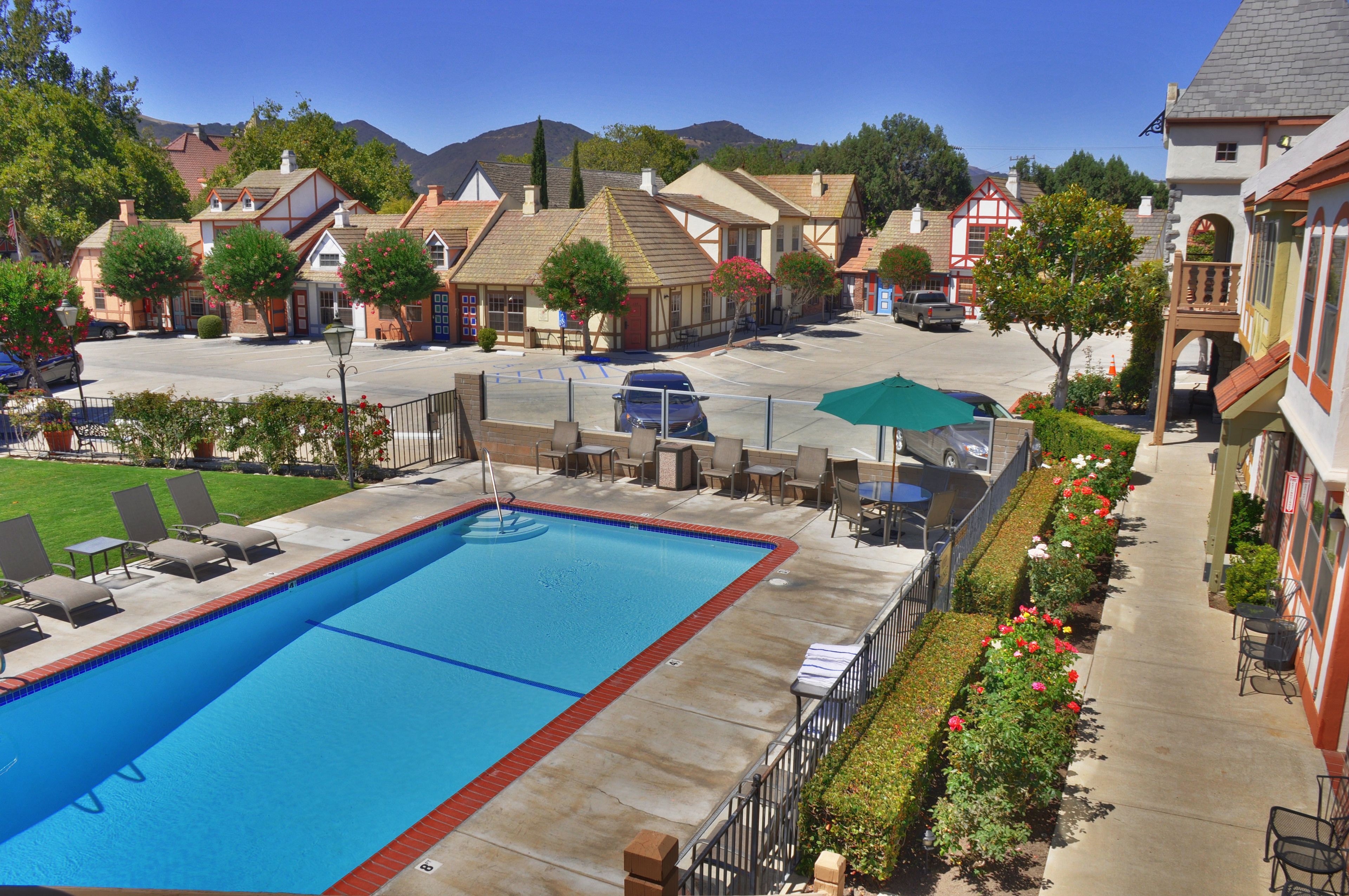 A swimming pool with lounge chairs, a covered patio area, and a view of surrounding buildings.