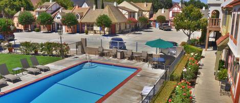 A swimming pool with lounge chairs, a covered patio area, and a view of surrounding buildings.