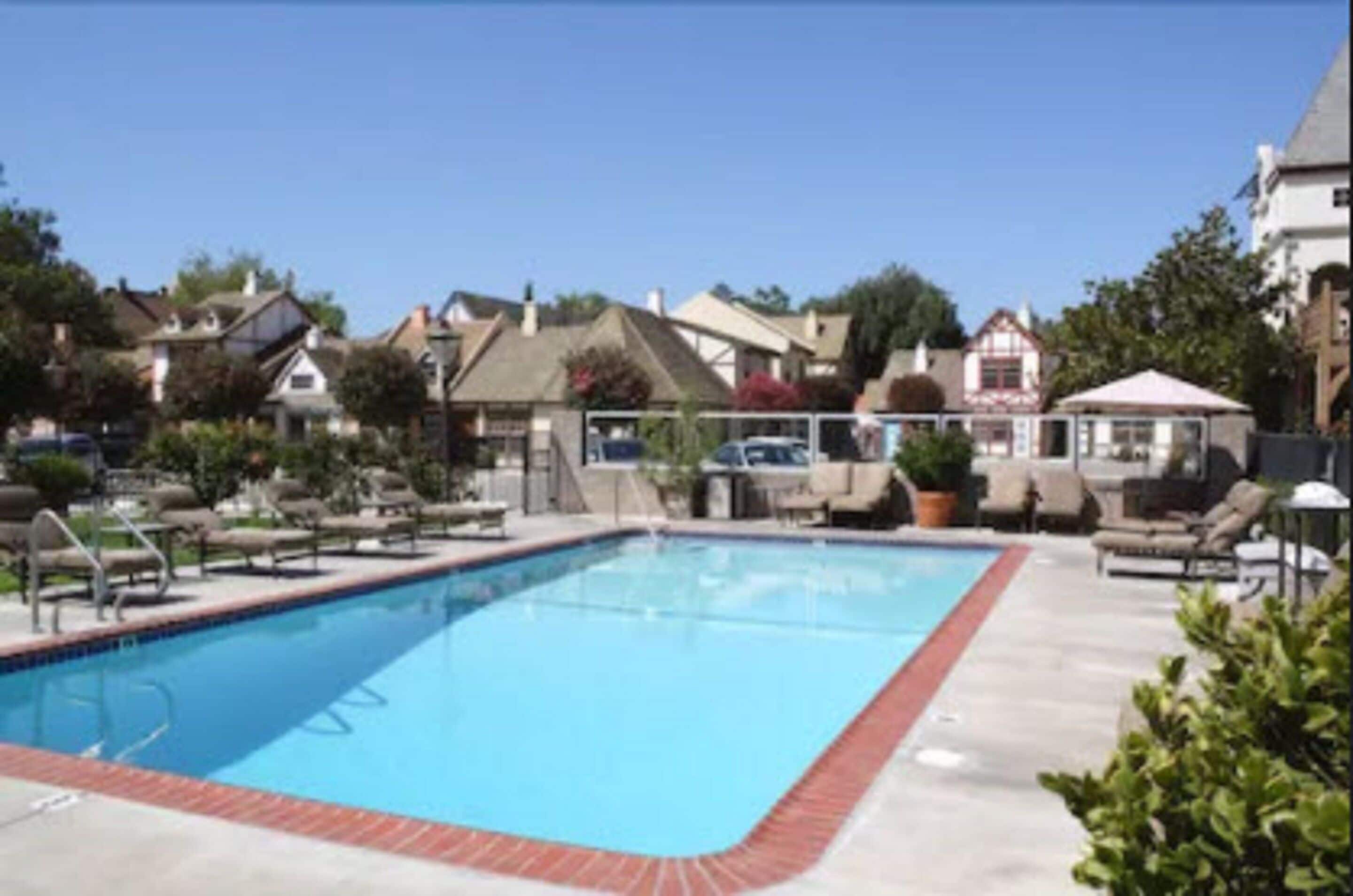 A rectangular pool with a red border, surrounded by lounge chairs and a gazebo.