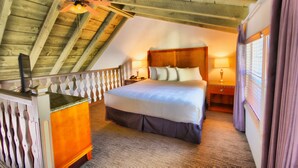 A bedroom with a sloped ceiling, a bed with multiple pillows, a nightstand, a lamp, and a wooden dresser. - Royal Copenhagen Inn (Solvang)