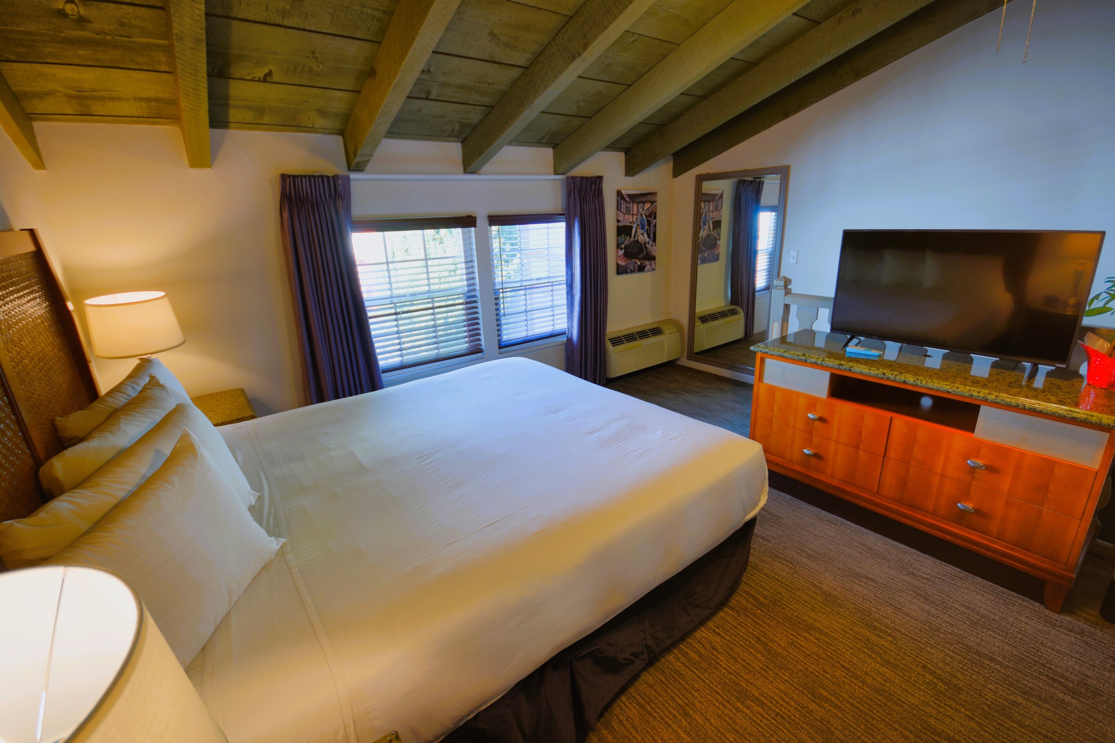 A hotel room with a large bed, a wooden dresser, a television, and a window with curtains.
