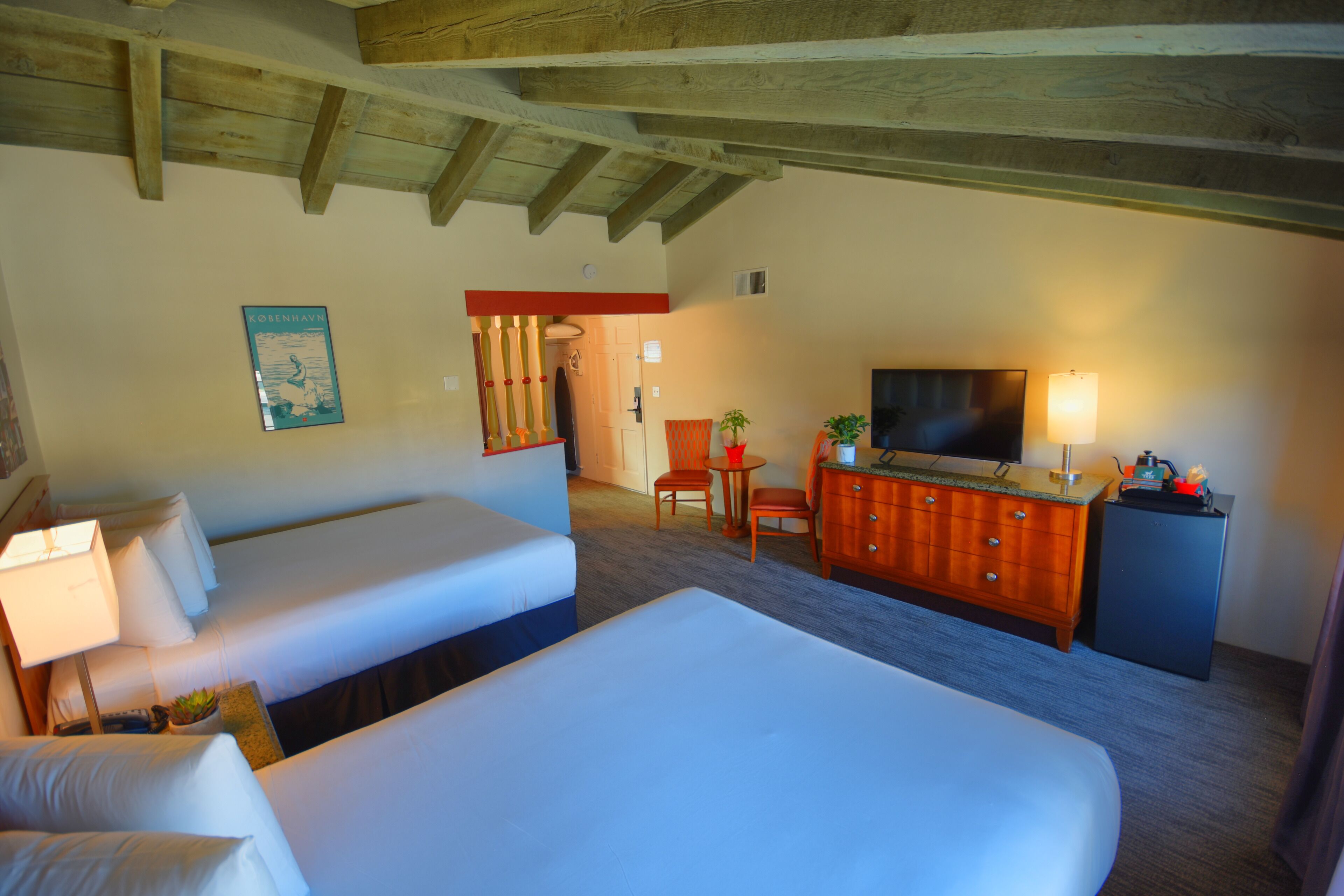 Une chambre d’hôtel avec deux lits, une commode en bois, un téléviseur et une petite table avec des chaises.