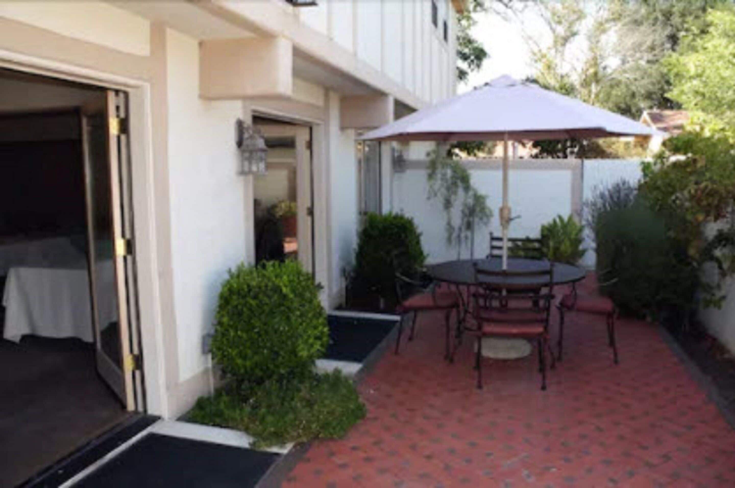 A patio with a table and chairs, a covered umbrella, and a small garden area.