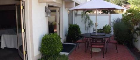 A patio with a table and chairs, a covered umbrella, and a small garden area.