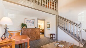 A cozy living room with a wooden dining table, chairs, a glass coffee table, and a staircase with a decorative railing. - Royal Copenhagen Inn (Solvang)