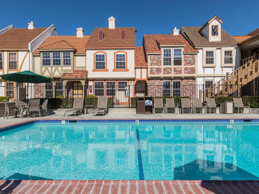 A swimming pool with lounge chairs and a covered seating area, surrounded by multi-story buildings with distinct architectural styles.