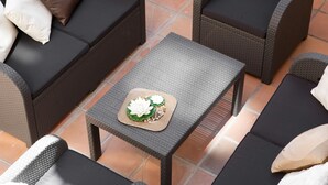 En patio med fletningsmøbler, herunder to sofaer og et lille bord med en dekorativ genstand.