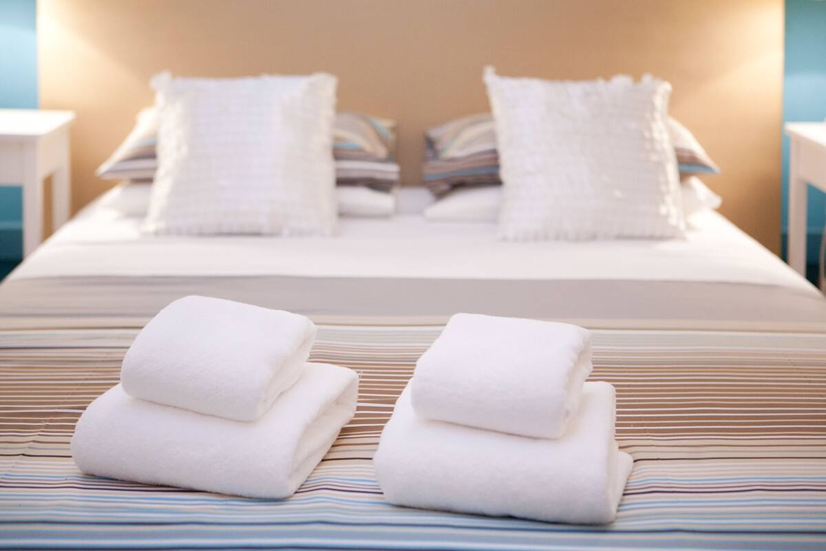 Una cama bien hecha con ropa de cama a rayas y dos toallas blancas dobladas sobre ella.