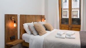 En pænt redt seng med hvide sengetøj og beige puder, et træhovedgærde og et sengebord med en lampe.