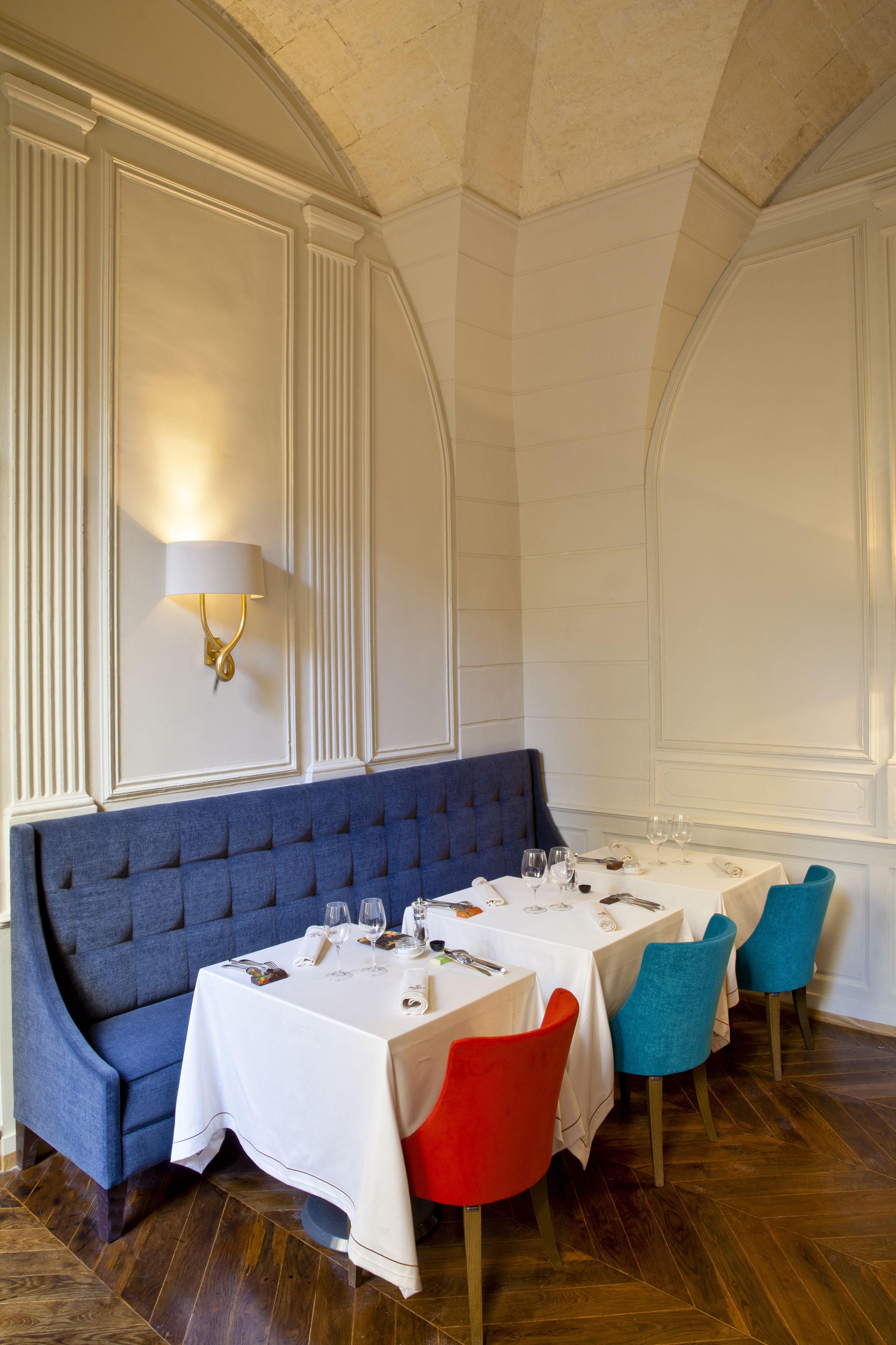 A dining area with a blue upholstered bench, white tables, and colorful chairs.