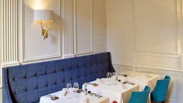 A dining area with a blue upholstered bench, white tables, and colorful chairs.