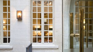A hotel room with a large window, a wall-mounted light fixture, and a glass door with a metallic handle. - La Maison d'Uzes (Uzès)