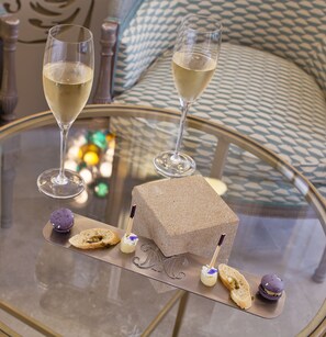 A glass table with two glasses of white wine, a square cake, and macarons. - La Maison d'Uzes (Uzès)