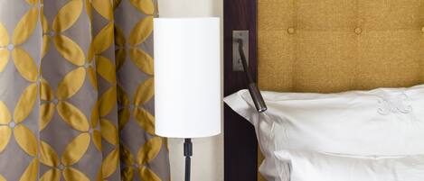 Ein Hotelzimmer mit einem Bett, einer Nachttischlampe, einem kleinen Tisch mit einem Buch und einem Vorhang mit Blätermotiv.
