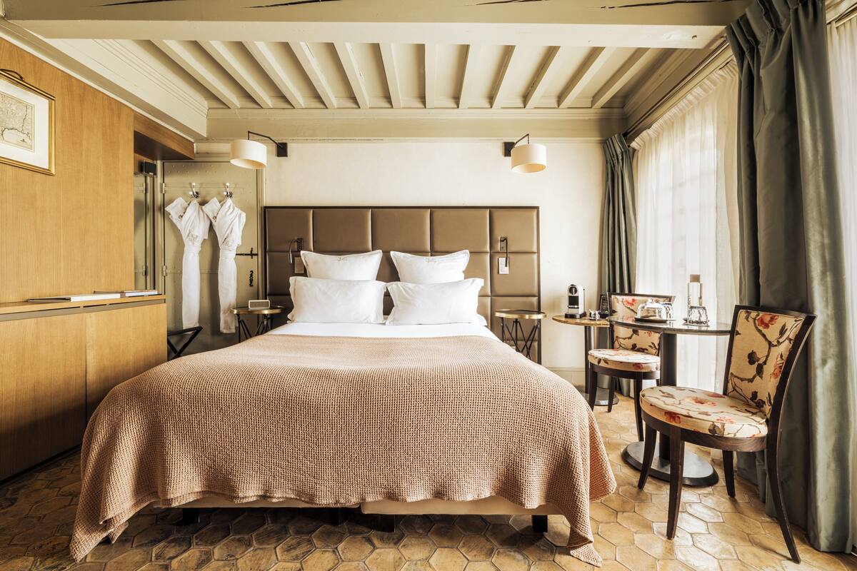 A hotel room with a large bed, a wooden wardrobe, a desk with a chair, and a window with curtains.