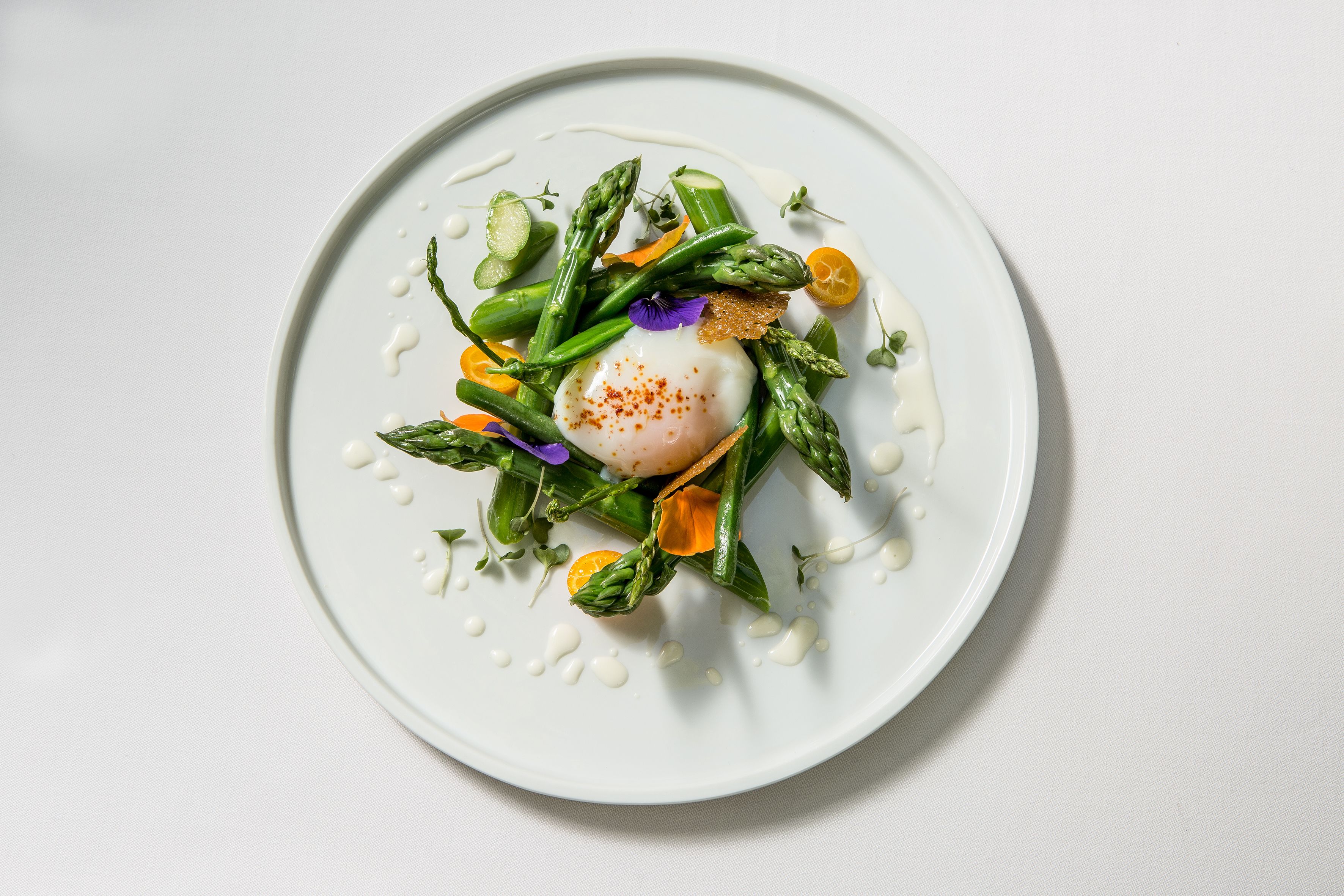 Une assiette blanche avec un œuf poché, des asperges et des tranches d’orange.
