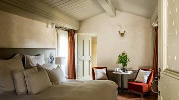 Ett hotellrum med en stor säng, två fåtöljer, ett litet bord med en växt och en dörr med ett dekorativt handtag.