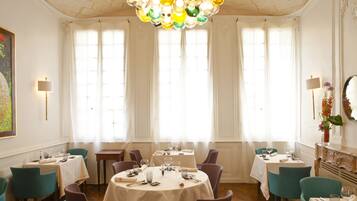 A dining area with round tables, teal chairs, and a chandelier.