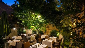 An outdoor dining area with tables and chairs, surrounded by trees and illuminated by string lights. - La Maison d'Uzes (Uzès)