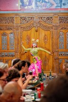 Un artista vestido con traje tradicional frente a un decorado de madera ornamentado.