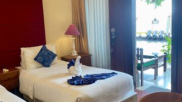 A hotel room with two beds, a nightstand, a lamp, and a view of the outdoor seating area.