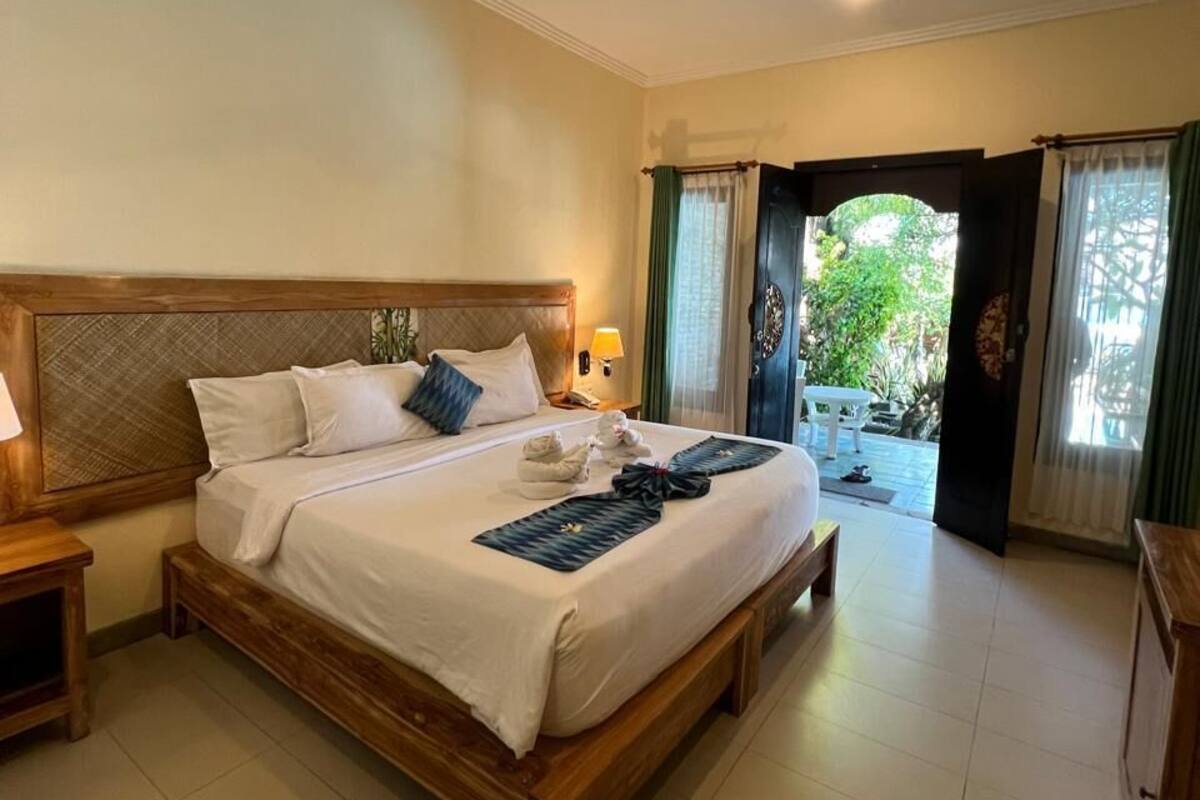 Habitación de hotel con una cama grande, un ventilador de techo, una mesita de noche y vistas al exterior.