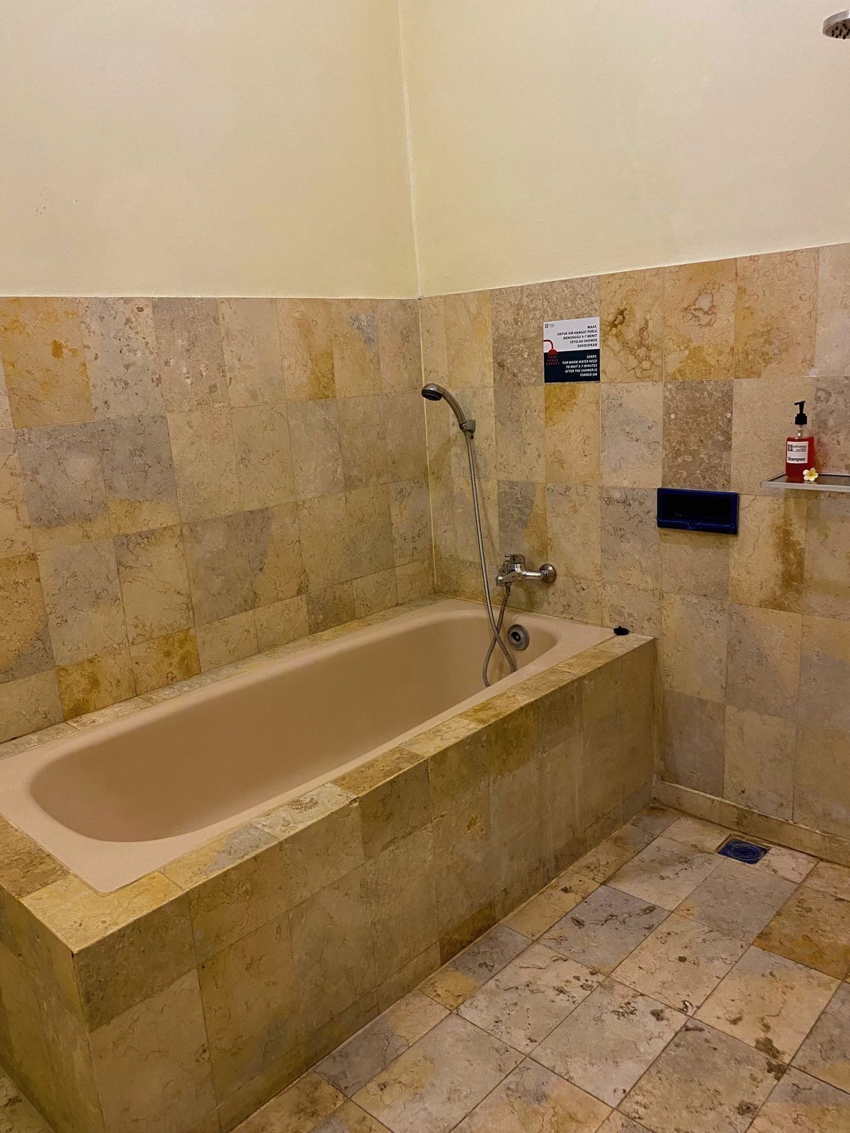 A bathroom with a freestanding bathtub, a showerhead, and a hand soap dispenser on a shelf.
