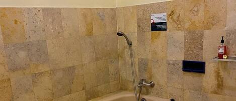 A bathroom with a freestanding bathtub, a showerhead, and a hand soap dispenser on a shelf.