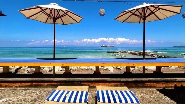 A beachside lounge with two umbrellas, a pool, and lounge chairs. - Ashyana Candidasa (Karangasem)