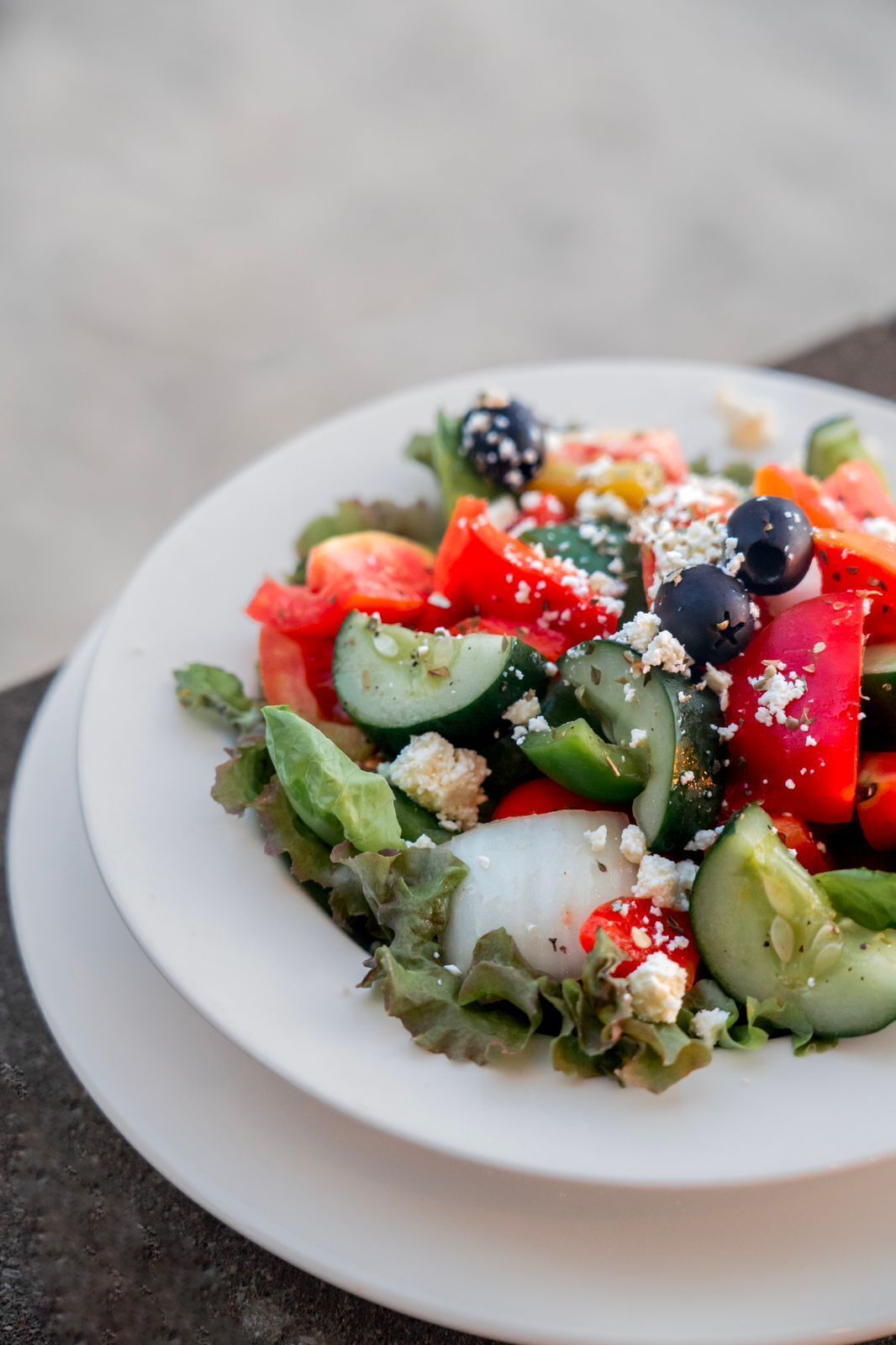 A white plate with a salad containing cucumbers, tomatoes, and black olives.