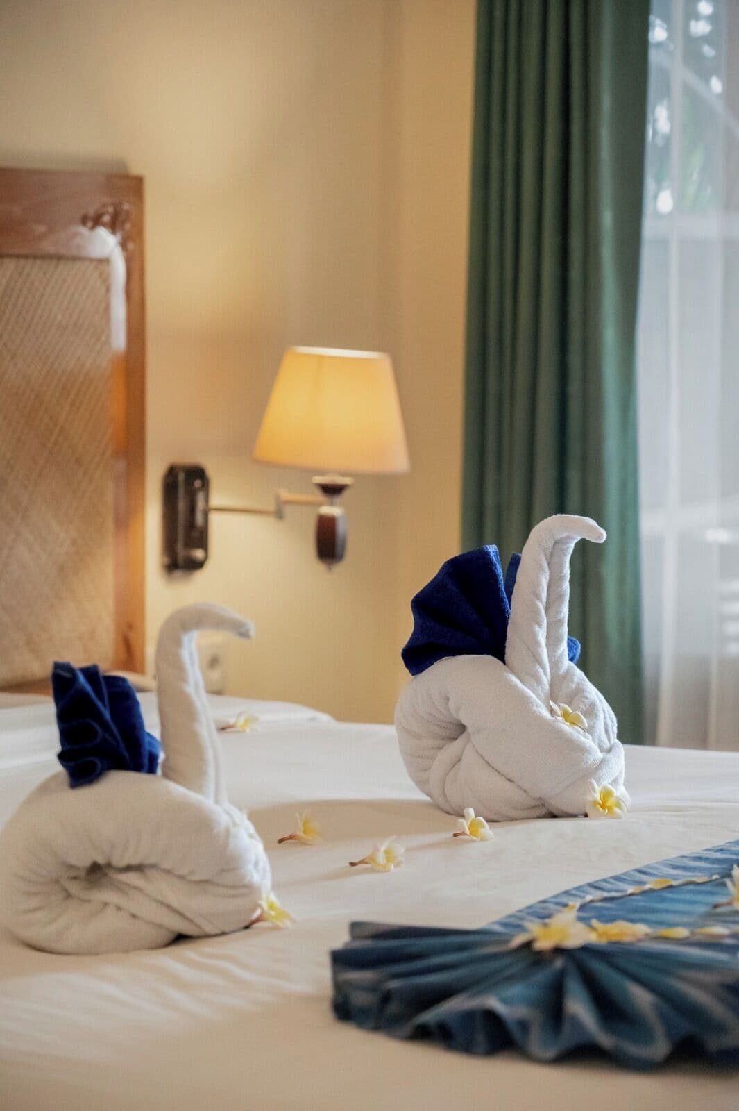 A hotel room with a bed, a lamp, and two towels shaped like swans.