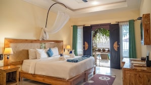 A well-lit bedroom with a large bed, bedside lamps, a ceiling fan, and a view of the outdoor area through an open door. - Ashyana Candidasa (Karangasem)