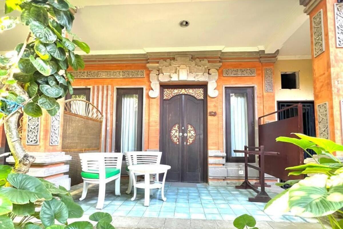 Entrada de un edificio con una puerta de madera oscura, dos sillas blancas y un suelo de baldosas.