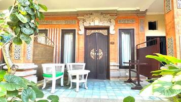 A building entrance with a dark wooden door, two white chairs, and a tiled floor.