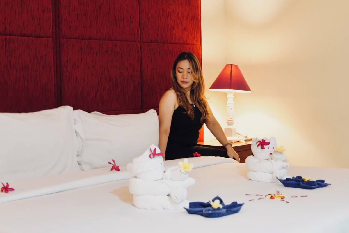 Una habitación de hotel con cama, almohadas, una mesita de noche, una lámpara y un peluche.