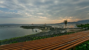 A coastal view with a wooden bench, rocky shoreline, and distant mountains. - Ashyana Candidasa (Karangasem)