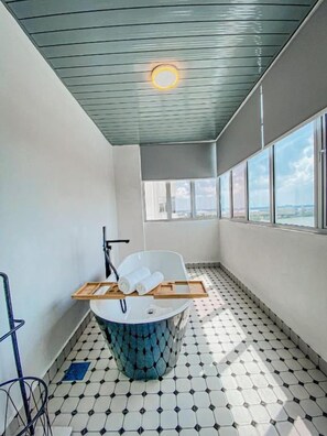 A modern bathroom with a bathtub, a towel rack, and a window providing a view of the cityscape. - Muar Traders Hotel (Muar)