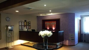 A reception area with a reception desk, a clock, framed certificates, and a vase with white flowers. - Muar Traders Hotel (Muar)